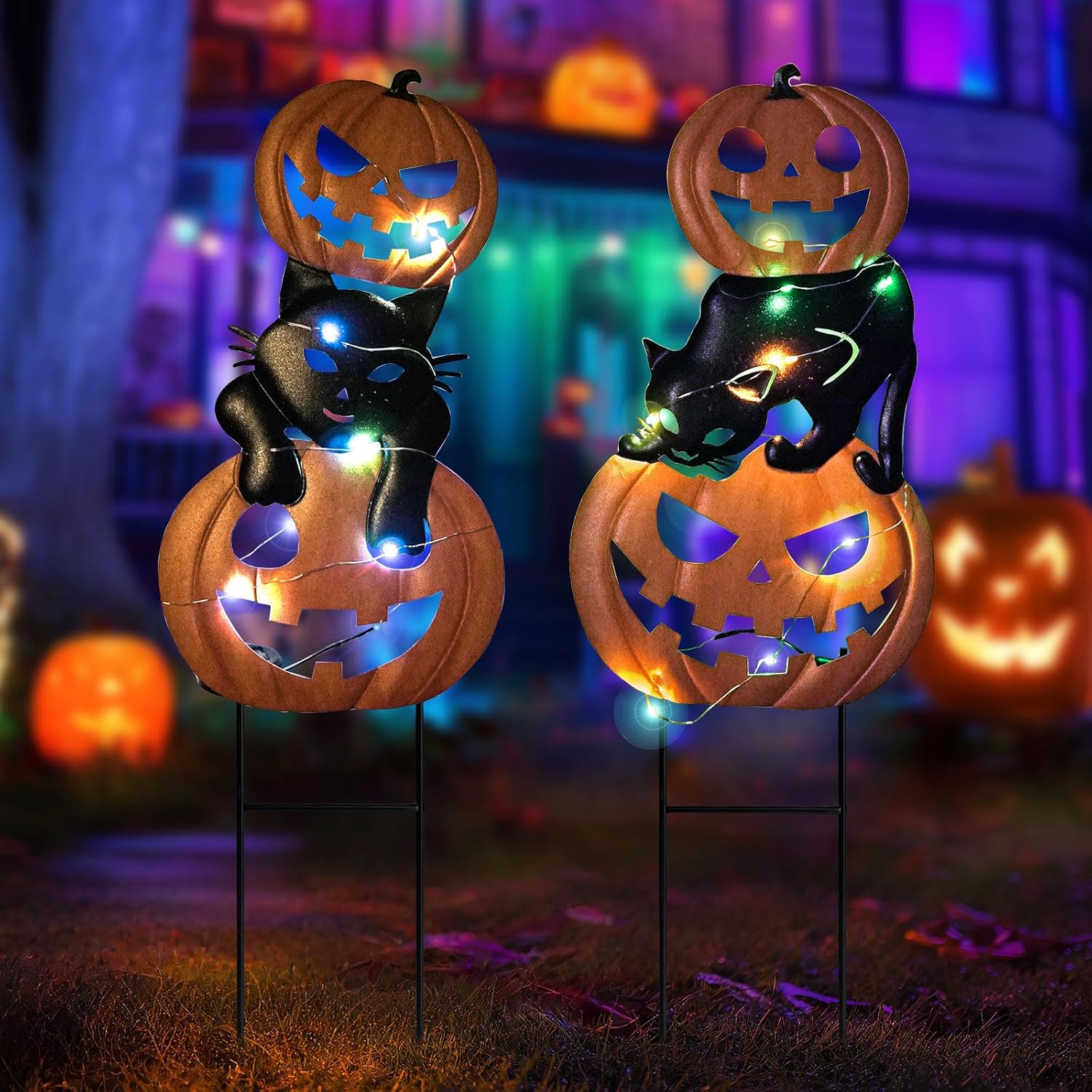 A pair of pumpkin and black cat garden stakes at night